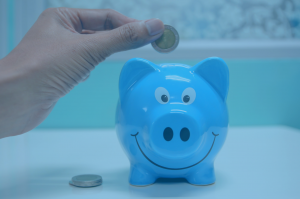 Regime Normal - Pessoa colocando moeda dentro de um cofre azul no formato de um porquinho.