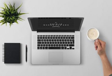 4 razões para automatizar a gestão fiscal e tributária do seu negócio - Mesa com notebook, caderno de anotações e um braço segurando uma xícara de café